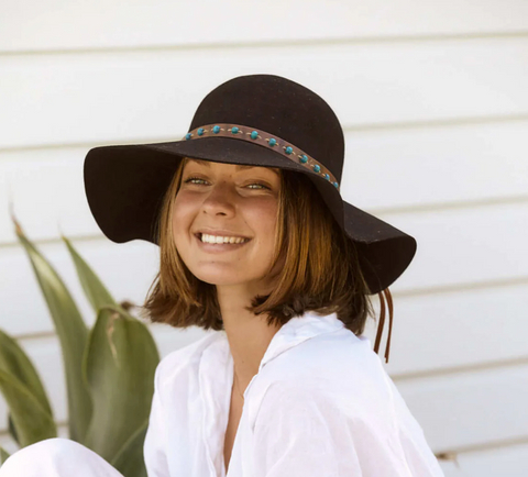 woman with short brown hat smiling while wearing a black floppy hat and a white top