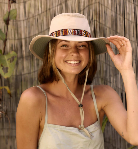 Woman smiles at the camera while wearing a boater hat with an aztec band and a tan tank top