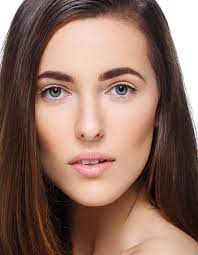 woman with dark brown hair and an oblong shaped face stares into the camera