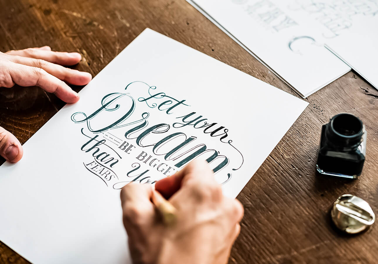 A person working on a hand lettering piece using ink.