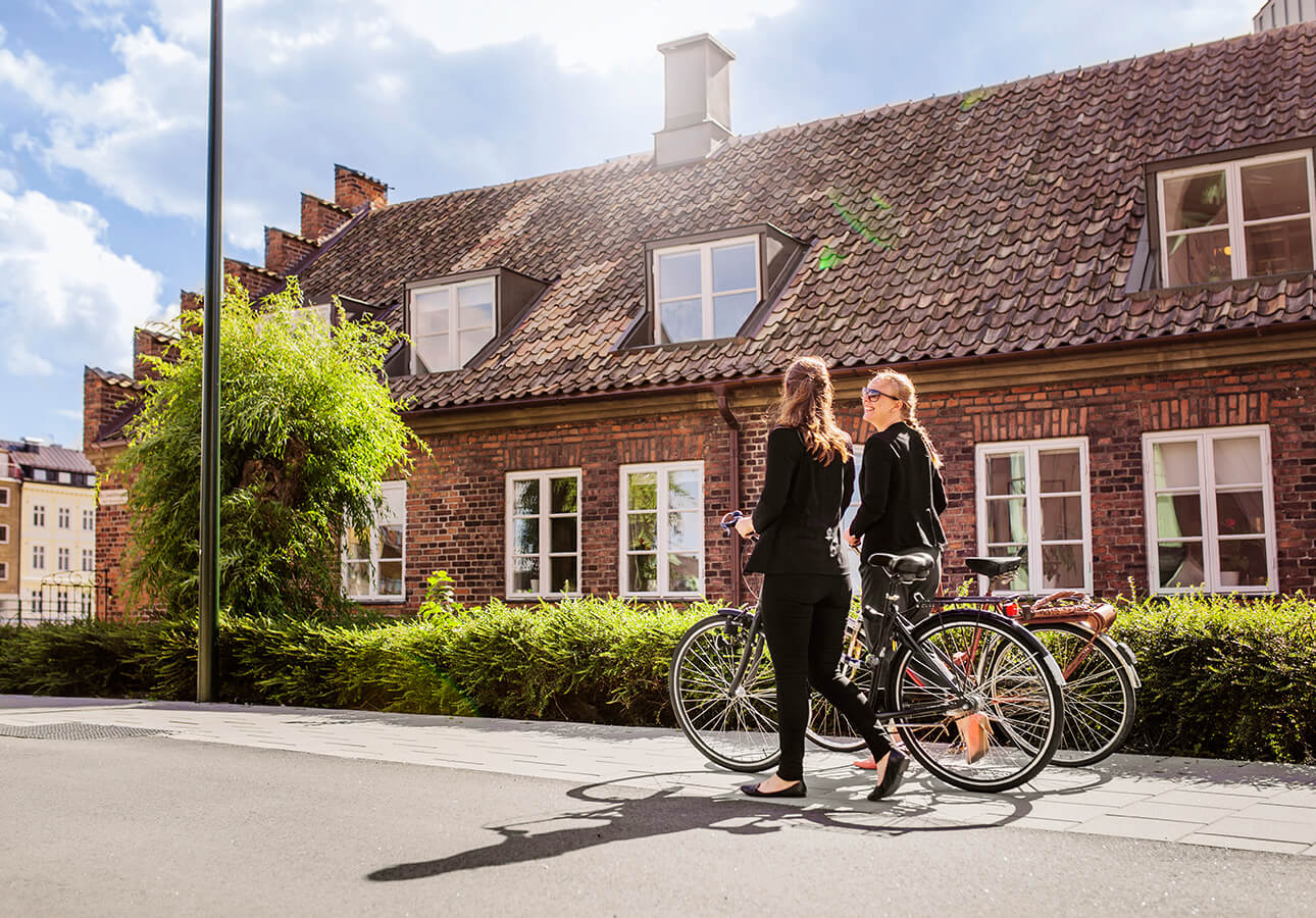 Two people walking with their bikes in a town on a sunny day.