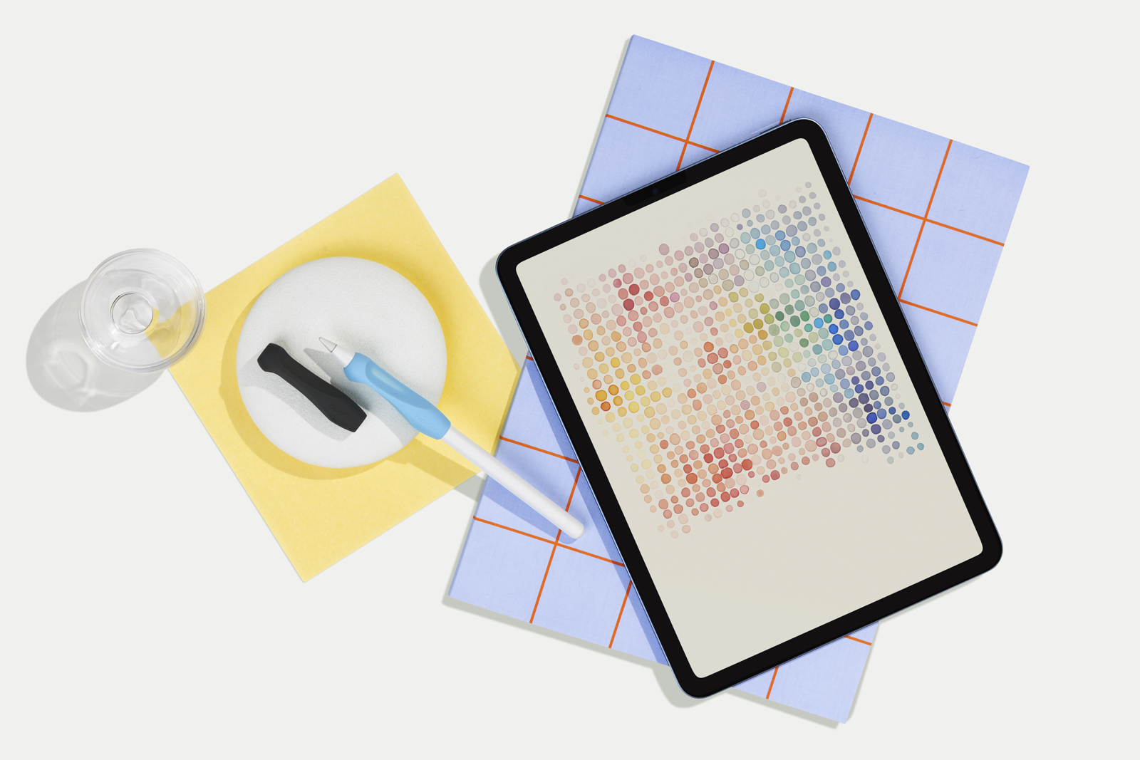 An iPad sits atop a mat with a grid pattern. An Apple Pencil and Paperlike’s Pencil Grips are placed off to the side.