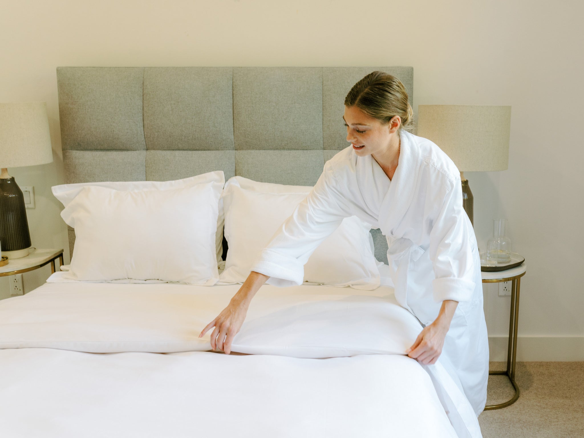Woman making the bed with white linens