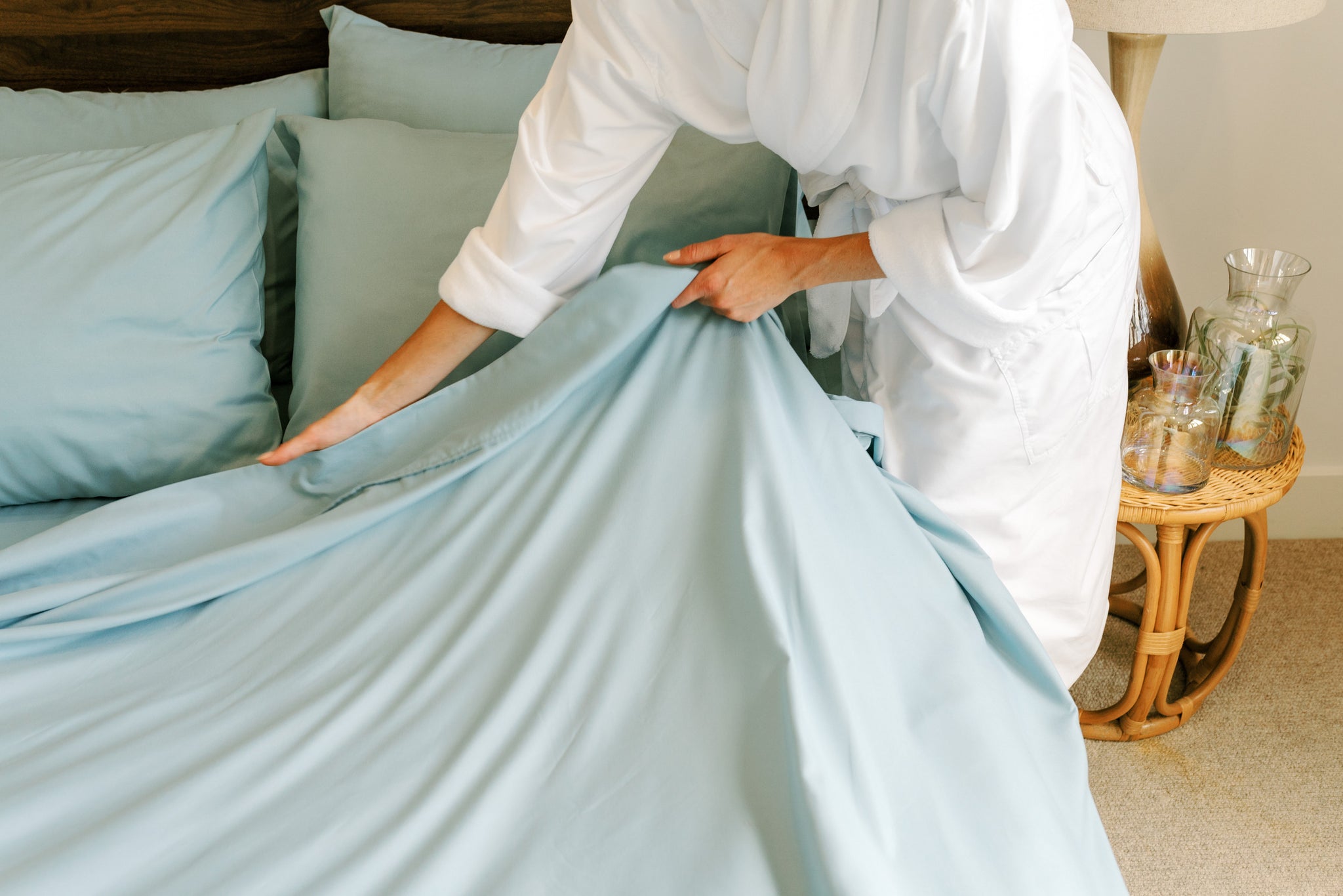 A woman making her bed without a comforter in summer.