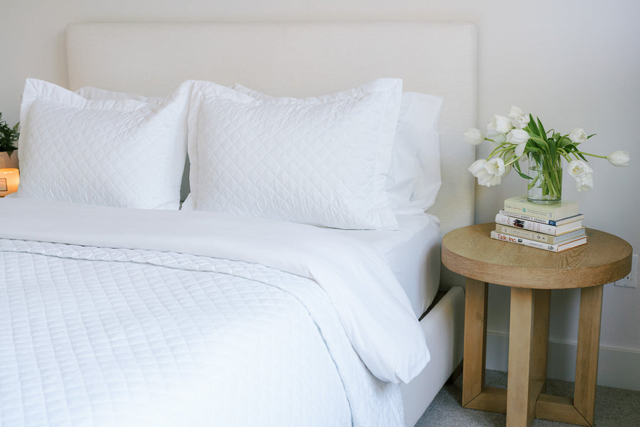 white made bed with side table with books and a plant