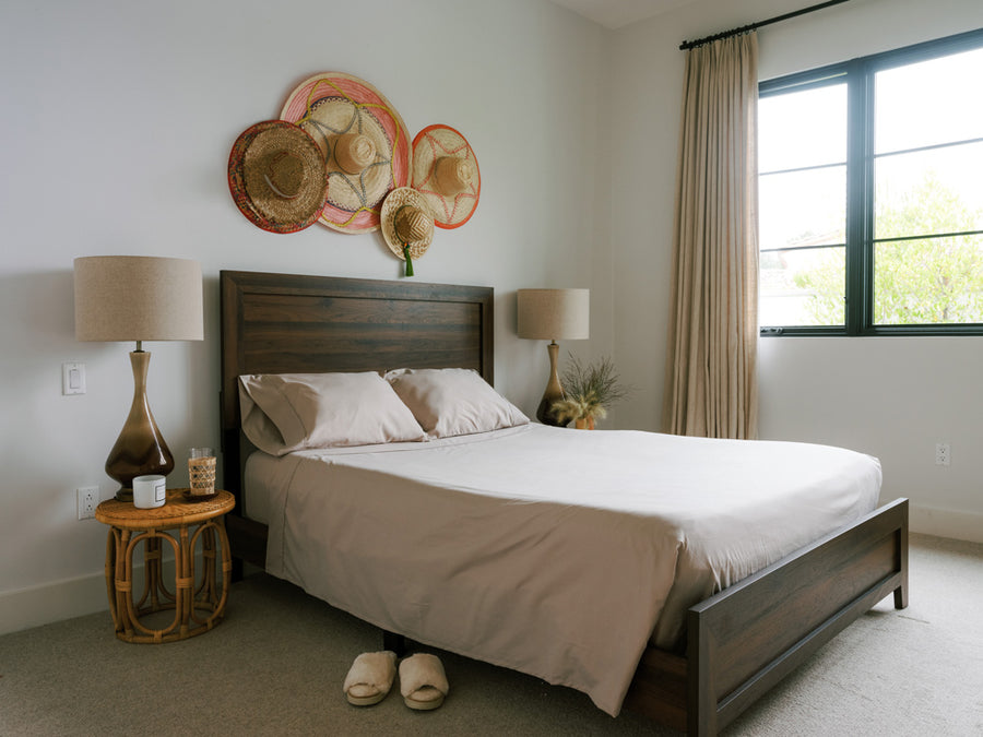 Made bed with side tables and hats on the wall above the bed