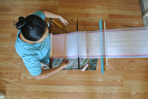 A resettled refugee from Burma operates a simple backstrap loom at her home in San Diego. She is an employee of Thread Spun, a local social enterprise that employs refugees to sew handmade board bags and accessories.