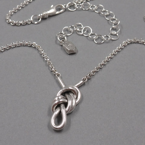 A sterling silver necklace with a figure 8 knot festoon at the center. The extender has a small rock charm at the end - from Forged Mettle Jewelry
