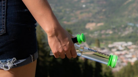 Glass bong with green res caps in hand of girl wearing shorts hiking up a mountain