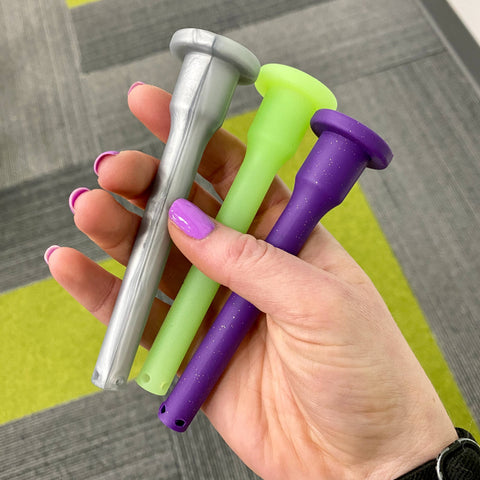 A white woman's hand holds 3 Ooze silicone diffused downstems. From left to right the colors are Stellar Silver, Glow Green, and Shimmer Purple.