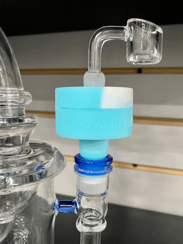 A close-up shot of a blue and white silicone reclaim catcher inserted into a clear and blue dab rig with a clear quartz 90 degree banger inserted in the top.