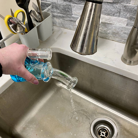 A blue Ooze Glyco bong is being dumped out into a stainless steel sink.