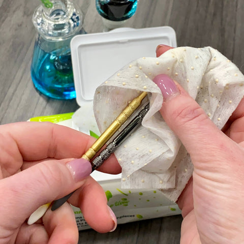 A white woman is cleaning two Ooze metal dab tools, gold and chrome, with an Ooze Resolution Res Wipe.