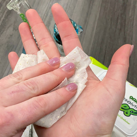 A white woman is cleaning resin off her palm with an Ooze Resolution Res Wipe.