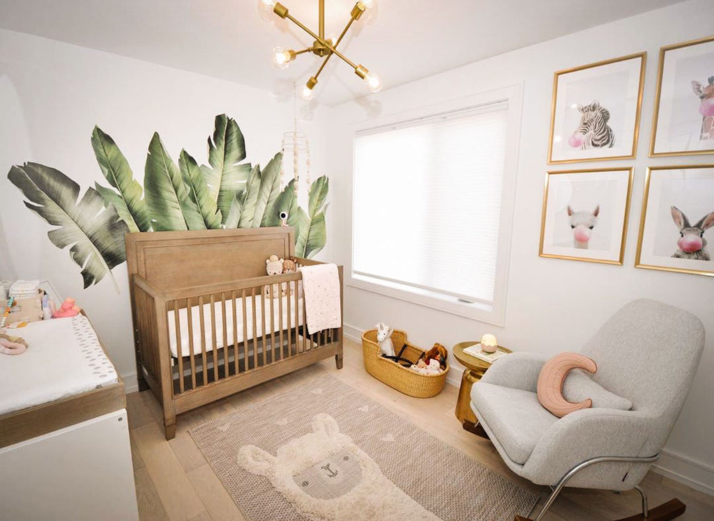 Nursery room with a wooden crib, brass chandelier, green leaf wall mural, and framed prints of baby animals blowing pink bubblegum bubbles