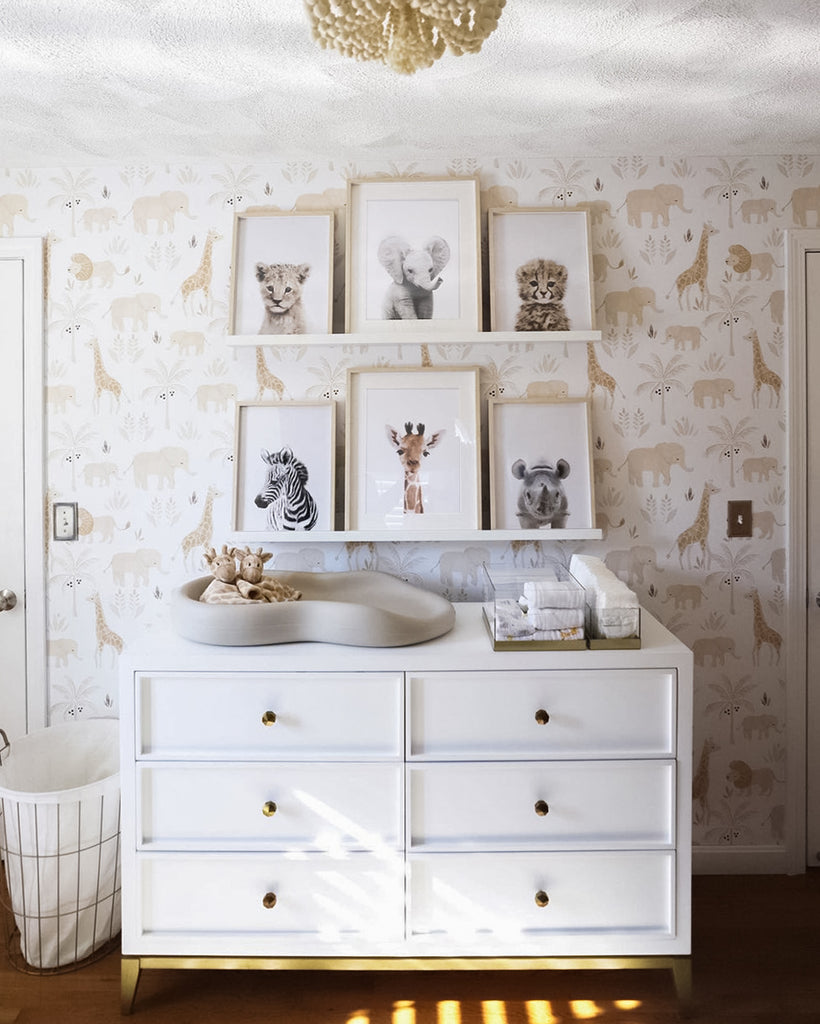 A nursery room with a dresser with changing table and supplies and framed baby animal prints on ledges above the dresser.