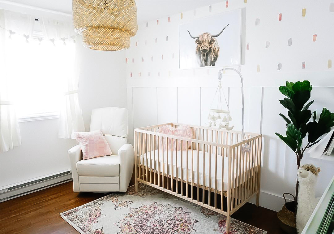 Nursery room with white walls and pink carpet and framed highland cow print above crib