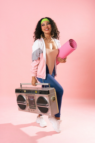 A woman dressed in an 80s style costume carrying a boombox and yoga mat
