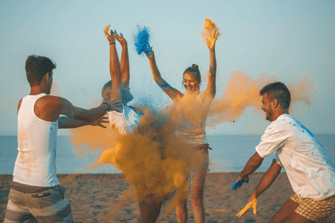 A group of people throwing colour powder in the air on the beach.