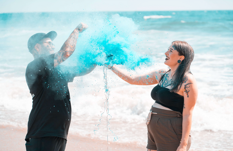 Couple on a beach popping a gender reveal balloon to reveal blue powder