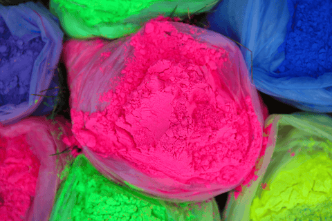 A close up image of bags of colour powder; pink, blue, green and neon yellow.