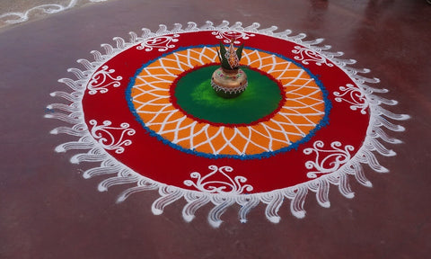 A rangoli art pattern on the ground made from coloured sand