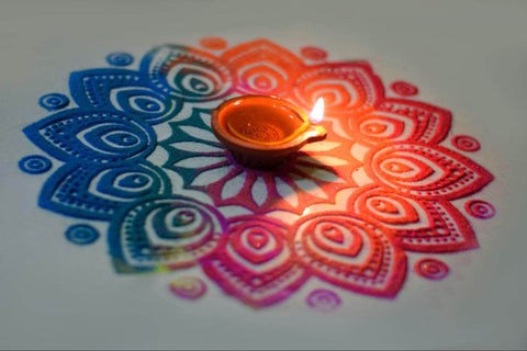 A mulitcoloured rangoli pattern made from coloured sand with a candle in the middle