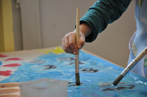 A child holding a paintbrush painting on paper