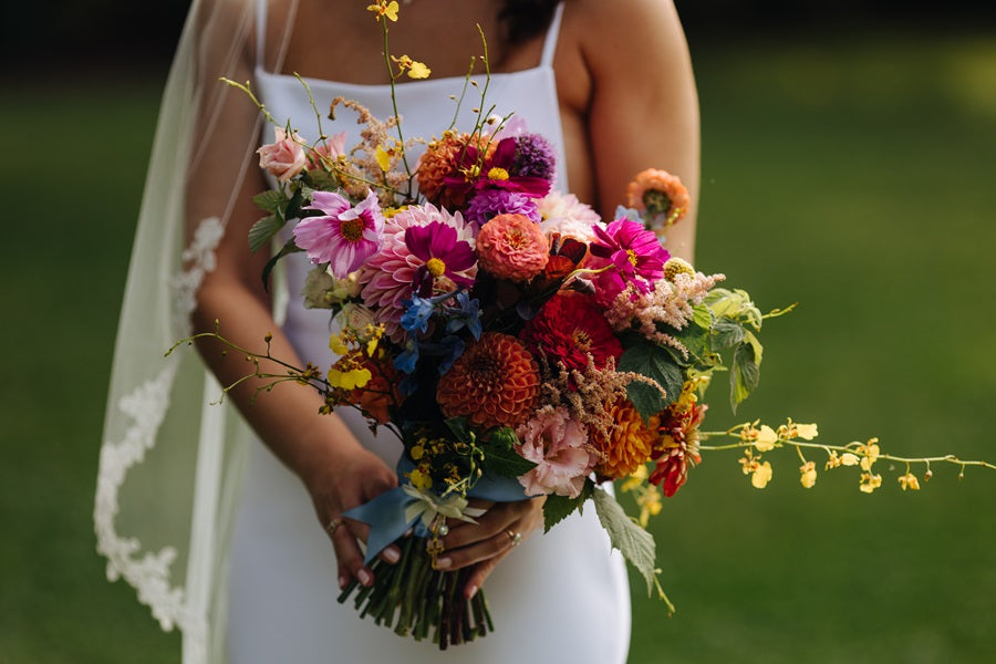 Bridal bouquet photo. Bride is holding a colorful bouquet with pinks, reds, oranges, greens, and accent colors.