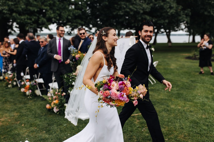 Bride and groom walking back down the aisle, bride holding a colorful floral bouquet.