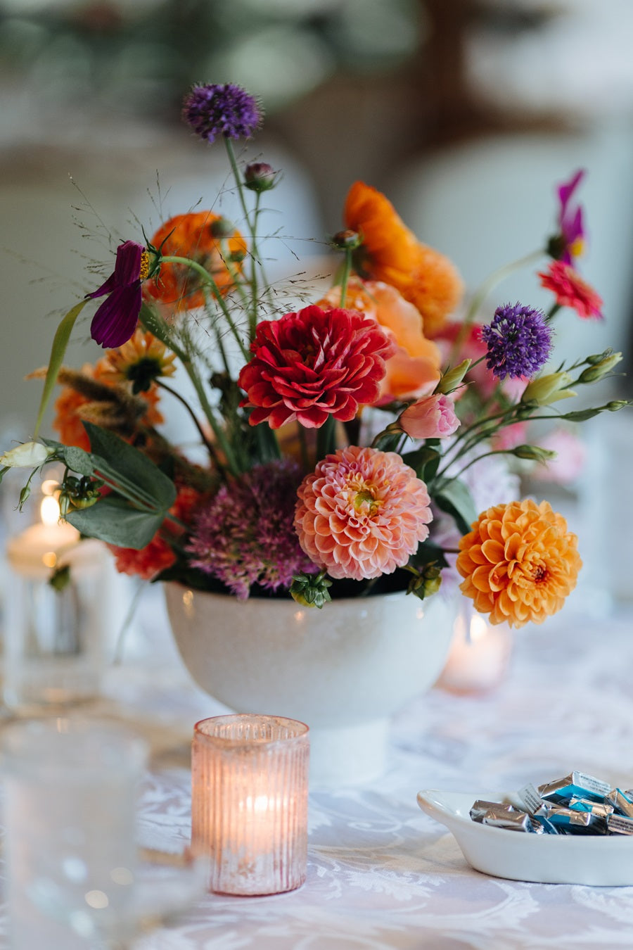 Close up shot of a floral centerpiece with dahlias and other accent florals. Colors are pink, red, orange, purple, and green.