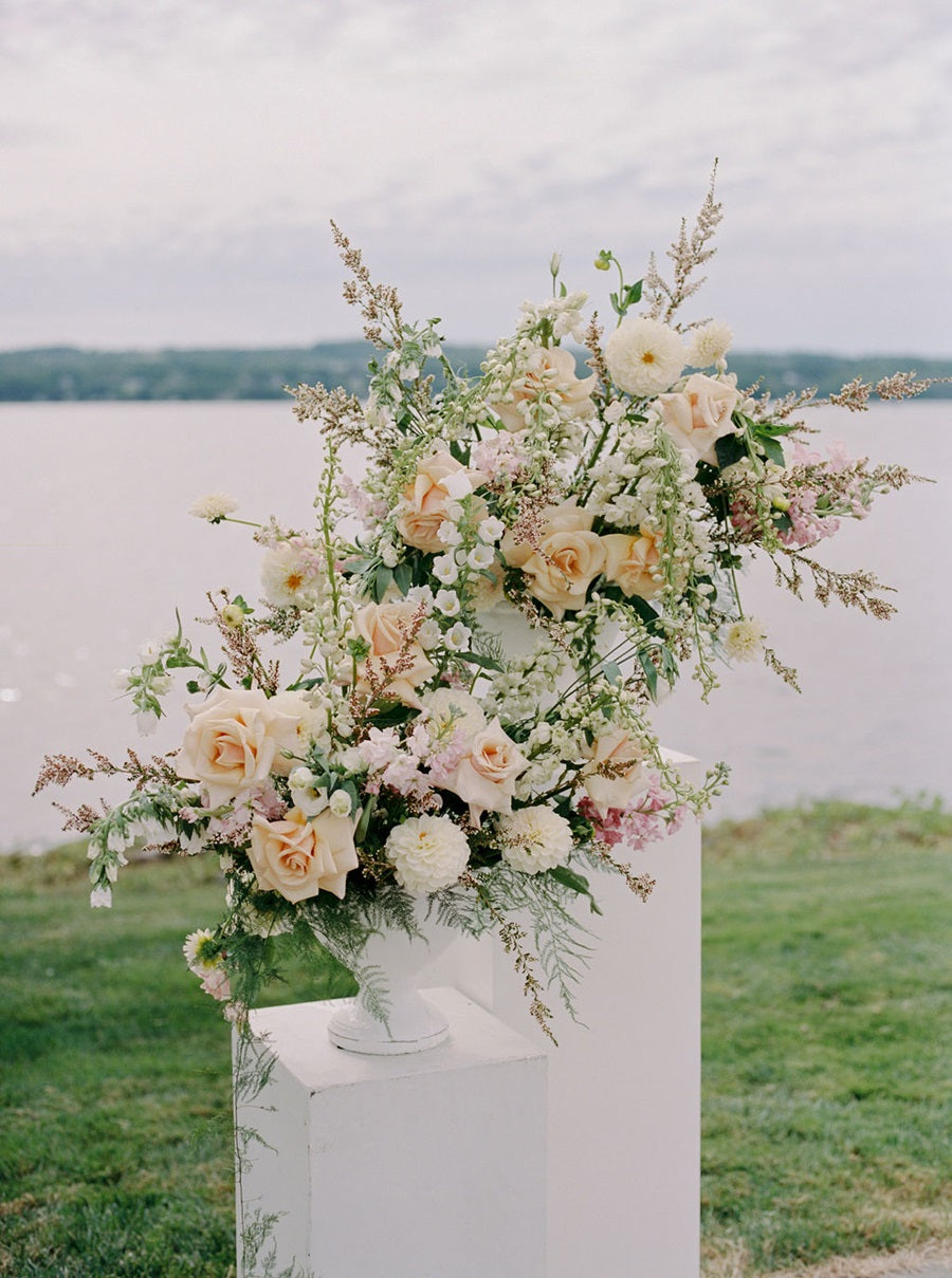 Large floral arrangements with a variety of textures and florals. Colors are white, peach, and pink, with green accents. Some flowers included are roses, dahlias, and snapdragons.