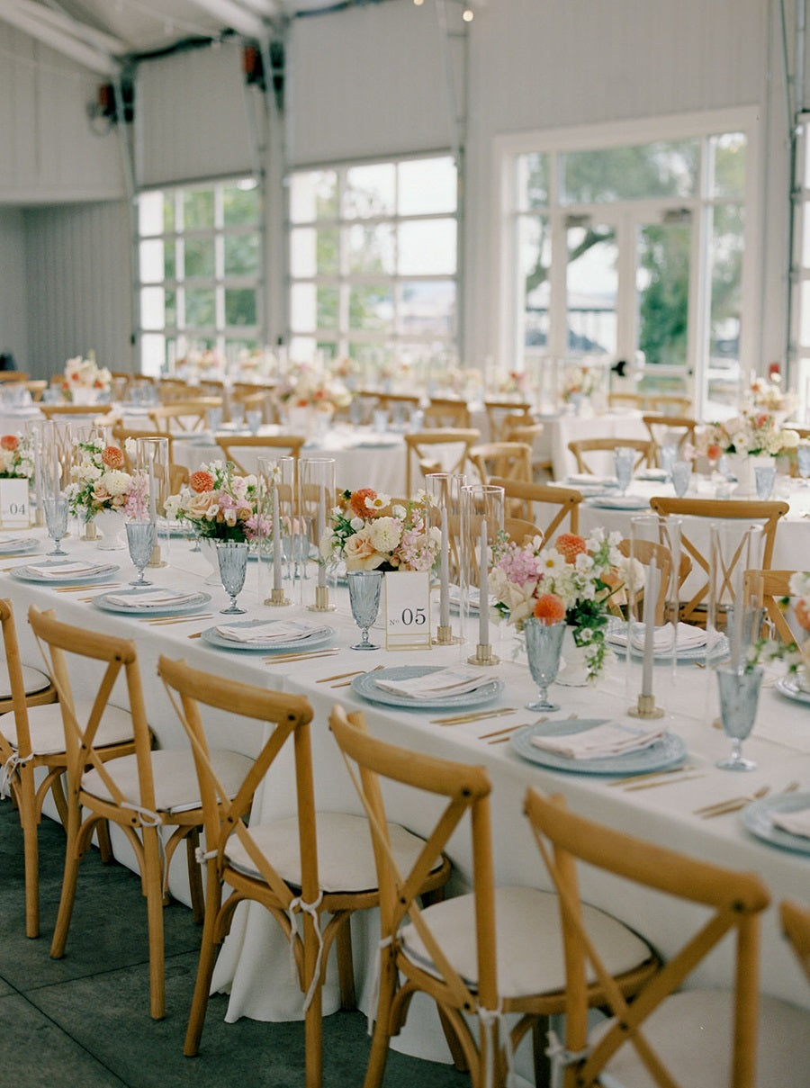 Reception room shot featuring blue and gold tableware with bright centerpieces made of pink, peach, white, and orange, with green accents.