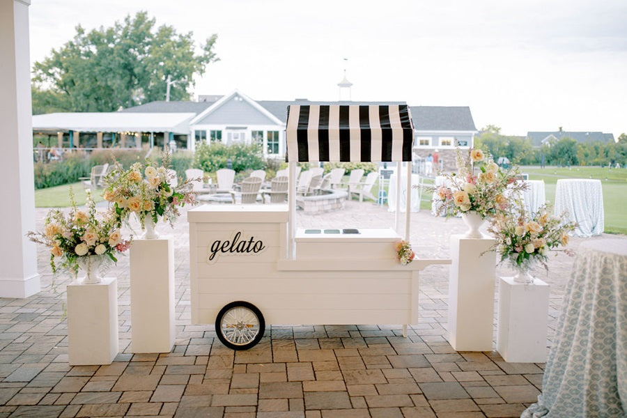 The gelato cart with a black/white awning. The floral arrangements from the ceremony have been reused to accentuate the cart.