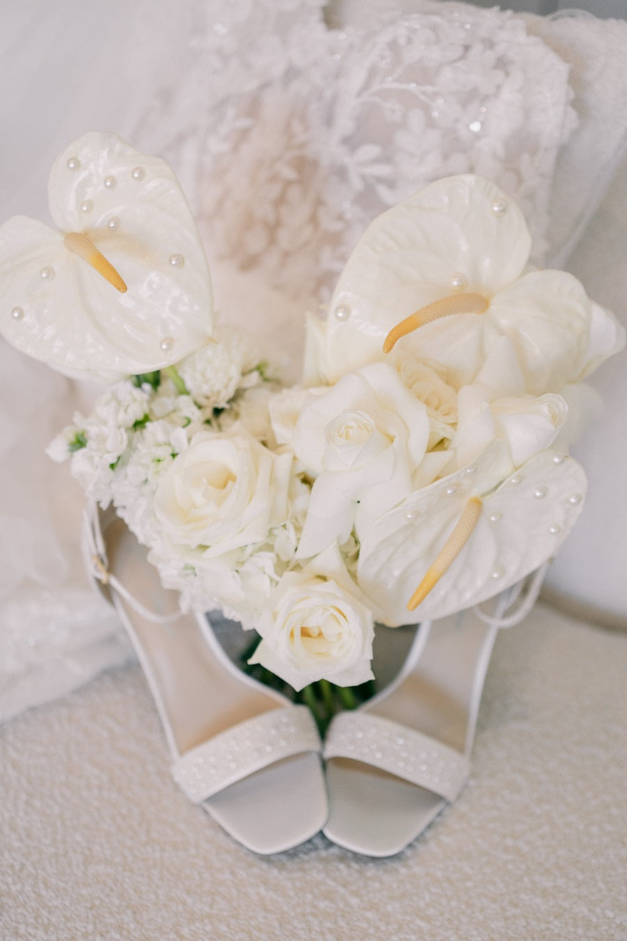 The bridal bouquet rest between the bride's shoes. The bouquet is full of roses and calathea, accented with pearls on the petals.