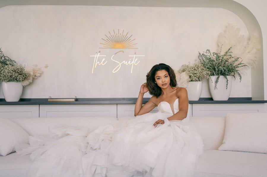 Bride lays sideways on a couch with dried floral arrangements in the background. The wall behind her reads "The Suite" in gold.
