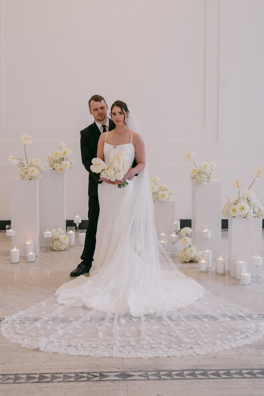 An Arbor Midtown photo shoot showing the bride and groom standing together surrounded by white floral arrangements with pearl accents. Bride's dress and veil, from Stella's Bridal, fans out in front of them.