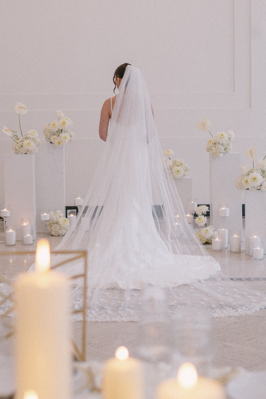 Bride stands with her back to the camera, florals in front of her and elements from the table decor showing behind her.