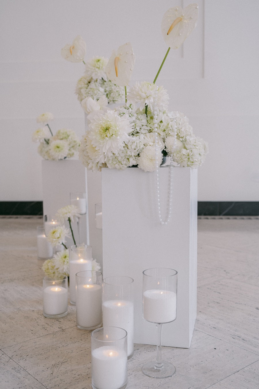 Close up on one of the floral pedestals. The arrangements are full of roses, calathea, and hydrangea. Accented with both hanging strands of pearls and individual pearls placed on the flower petals. Beaded candles line the base of the pedestal.