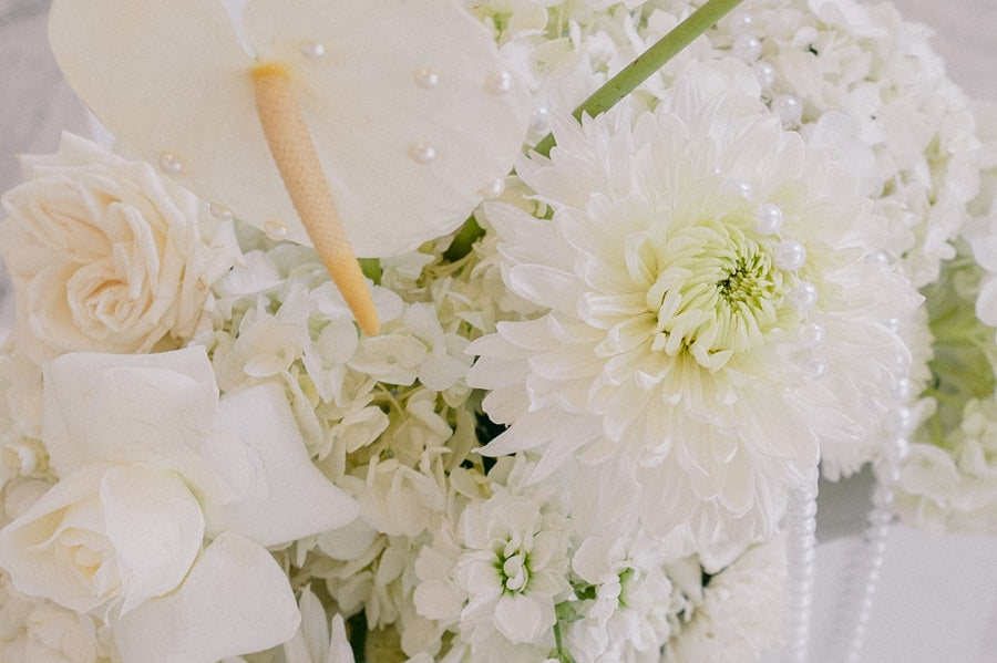 Close up on an arrangement with roses, hydrangea, mums, and calathea with pearl accents.