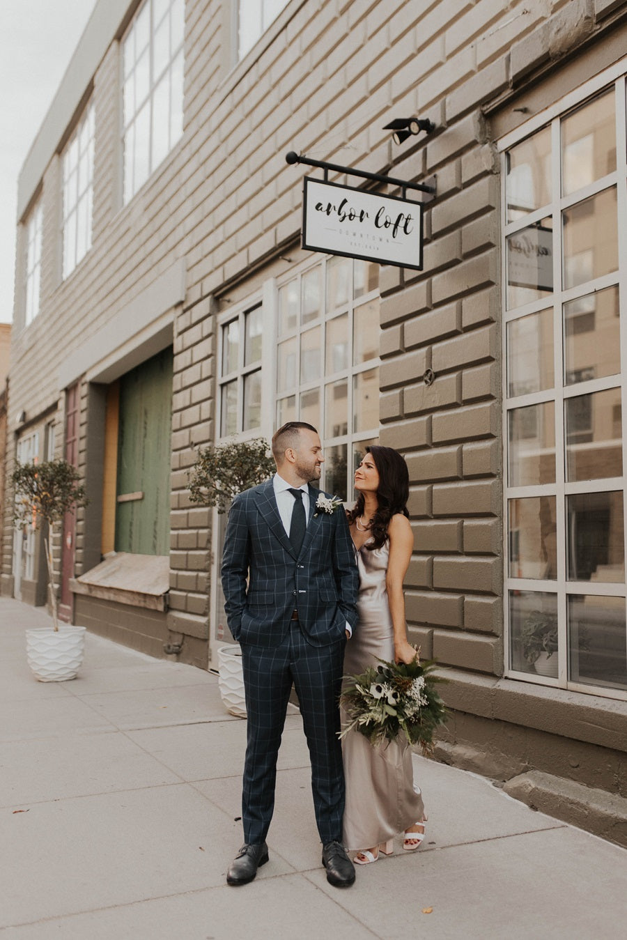Bride and groom pose outside of Arbor Loft. Bride is dressed in silver, holding her bridal bouquet.