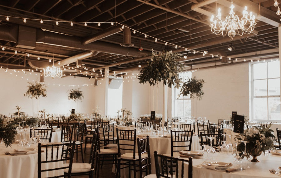 Reception shot highlighting the cohesive style. The tables have greenery/floral centerpieces, as well as raising greenery centerpieces that seem to "float" about the tables.