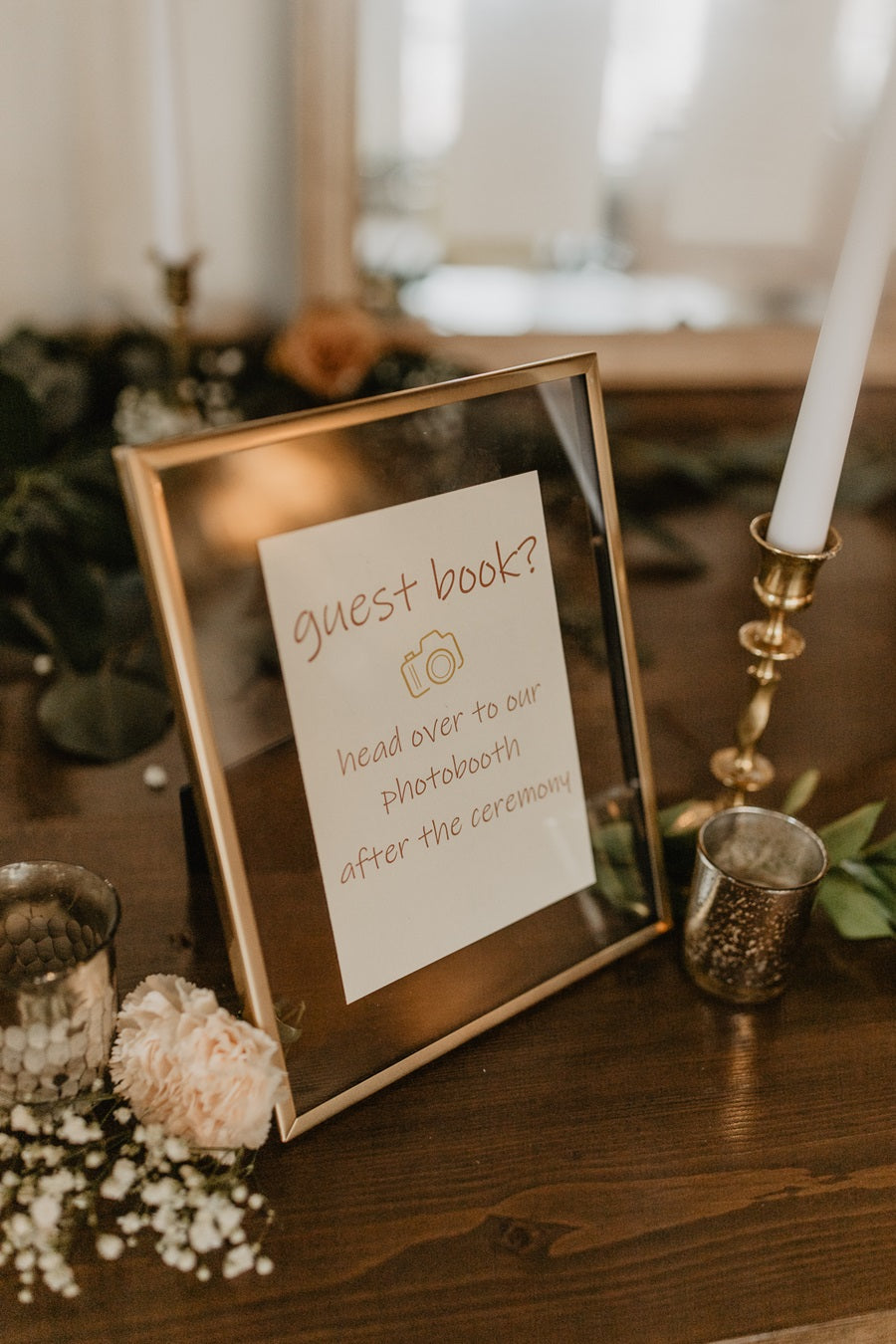 A small glass frame with "guest book?" "head over to our photobooth after the ceremony". Accented with loose florals, votives, and taper candles. 