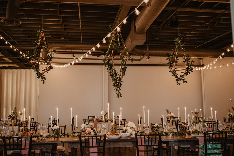 Rectangle table shot with hanging geometric pieces wrapped in greenery. Table is lush with greenery, candles, and table setting.