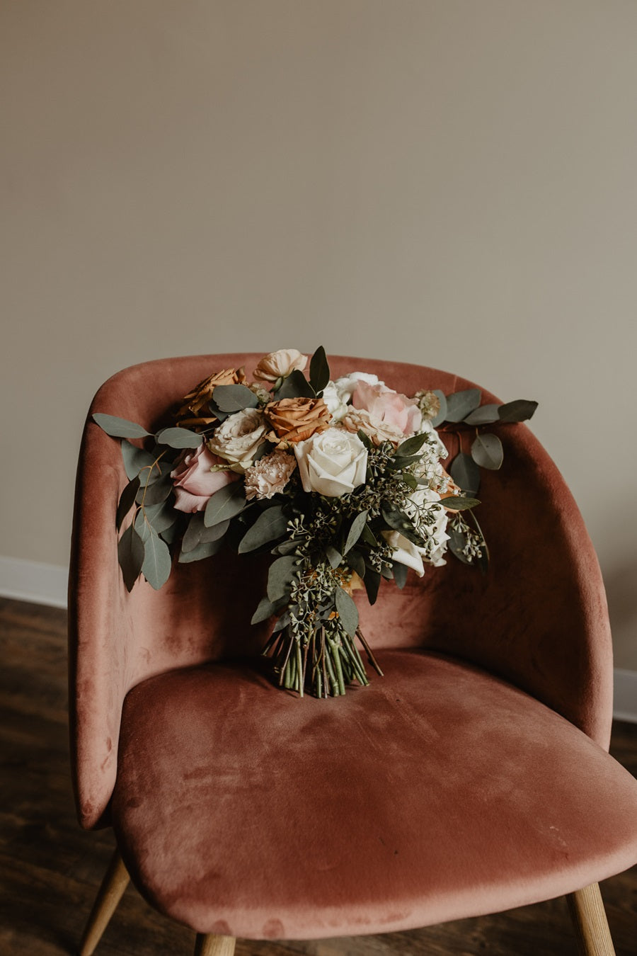 Bridal bouquet with peach, pink, and greenery, propped up on an orange suede chair.