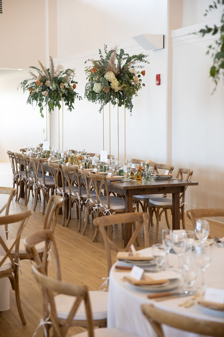 Reception photo showing the neutral tableware and high centerpieces. They are green with white and pampas grass accents.