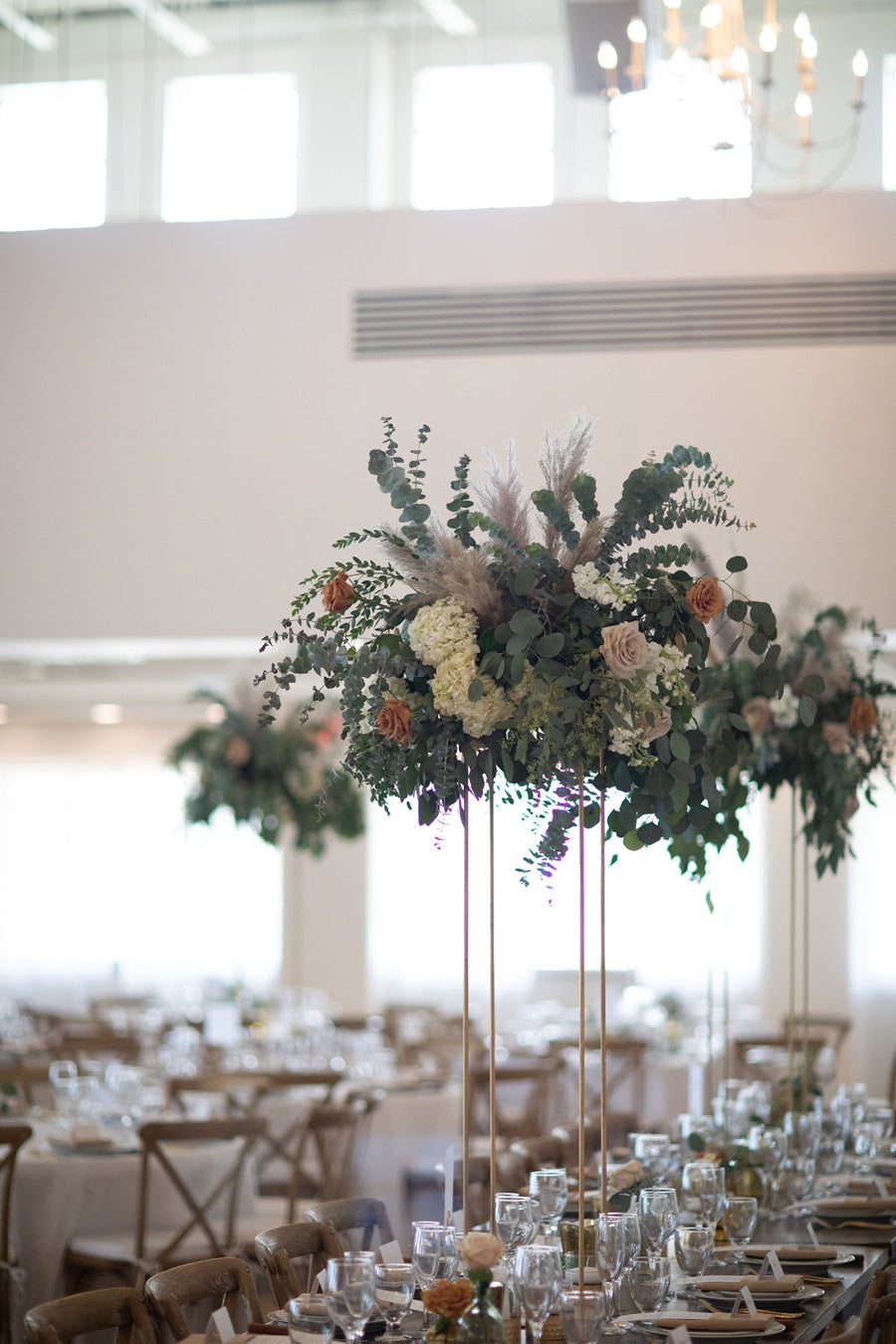 Detail shot of a raised centerpiece. Resting on a gold stand, it is lush with greenery, florals, and accents.