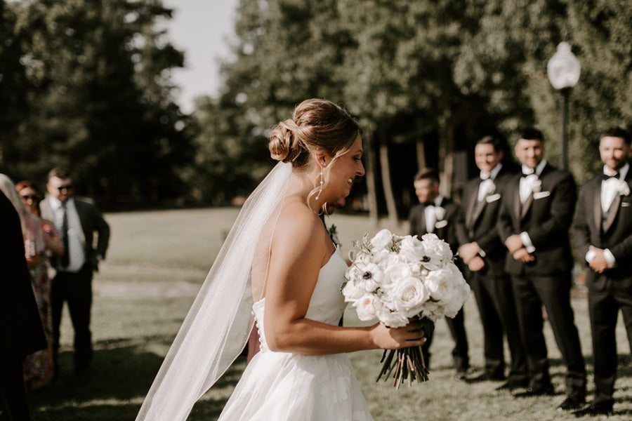 Bride walking down the aisle with her bridal bouquet. Groomsmen can be seen in the background.