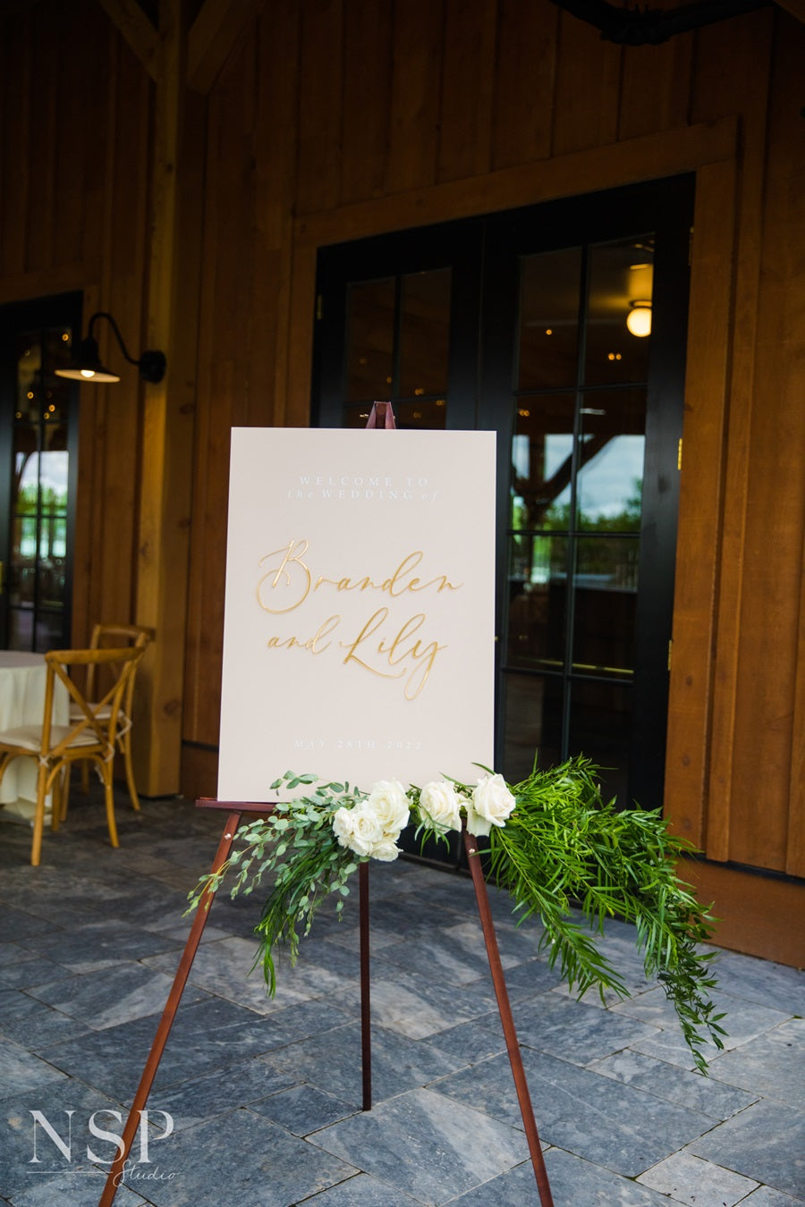 A welcome sign reading "Welcome to the wedding of Branden and Lily". Placed on an easel decorated with florals and greenery.