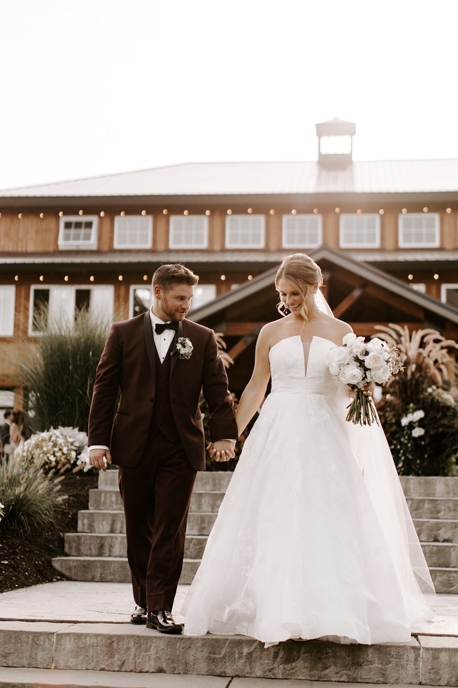 Bride and Groom walking down the steps in front of the Colloca Estate Winery. Bride holds a white w/black floral bouquet.